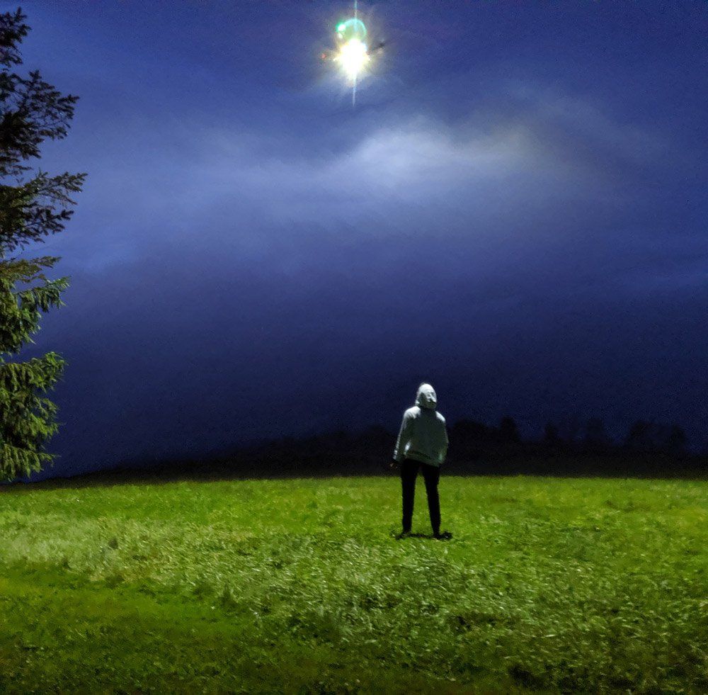 A person standing in a field at night looking at the moon