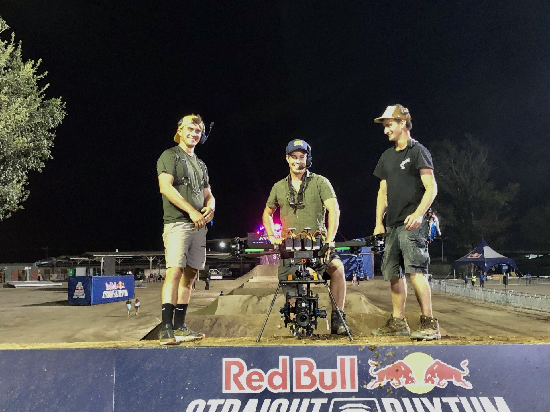 Three men are standing in front of a red bull sign