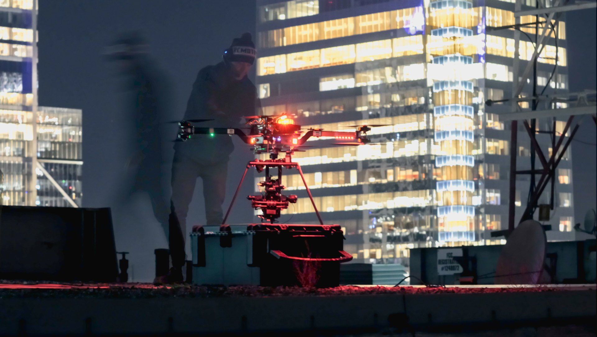 A man is standing on top of a building with a drone in the foreground.