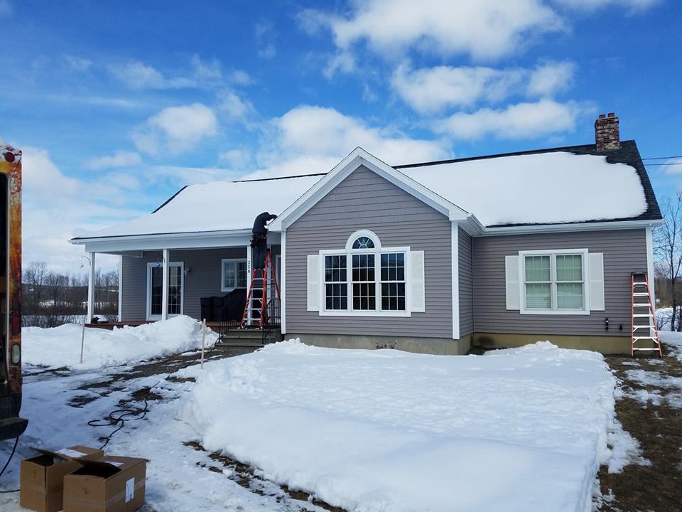 A house with snow on the ground and a ladder in front of it.
