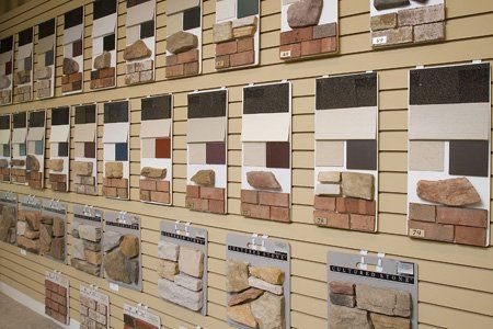 Display of tile samples on a slatwall in a showroom, showing beige, brown, and white stone patterns.