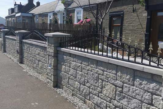 Brick wall with black rails on the top and gold accents. Row of houses in the background.