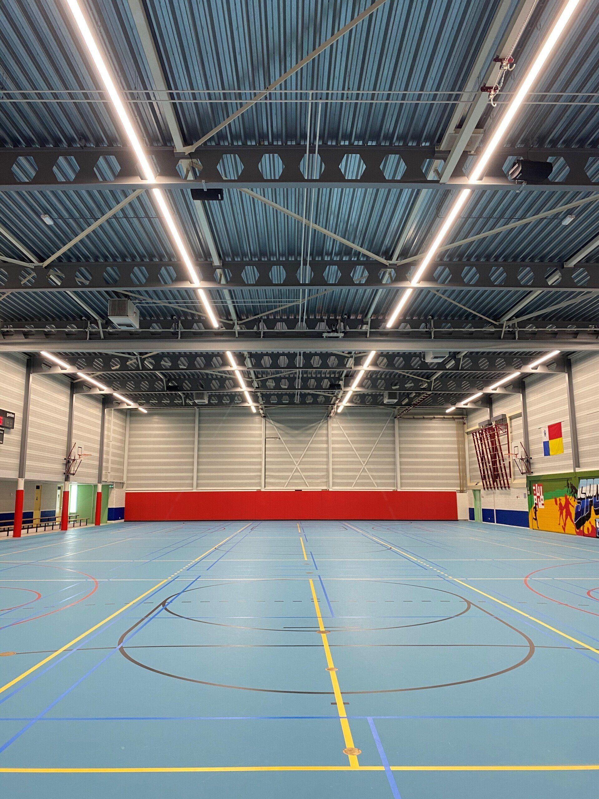 Een groot indoor basketbalveld met een blauwe vloer en een rode muur.