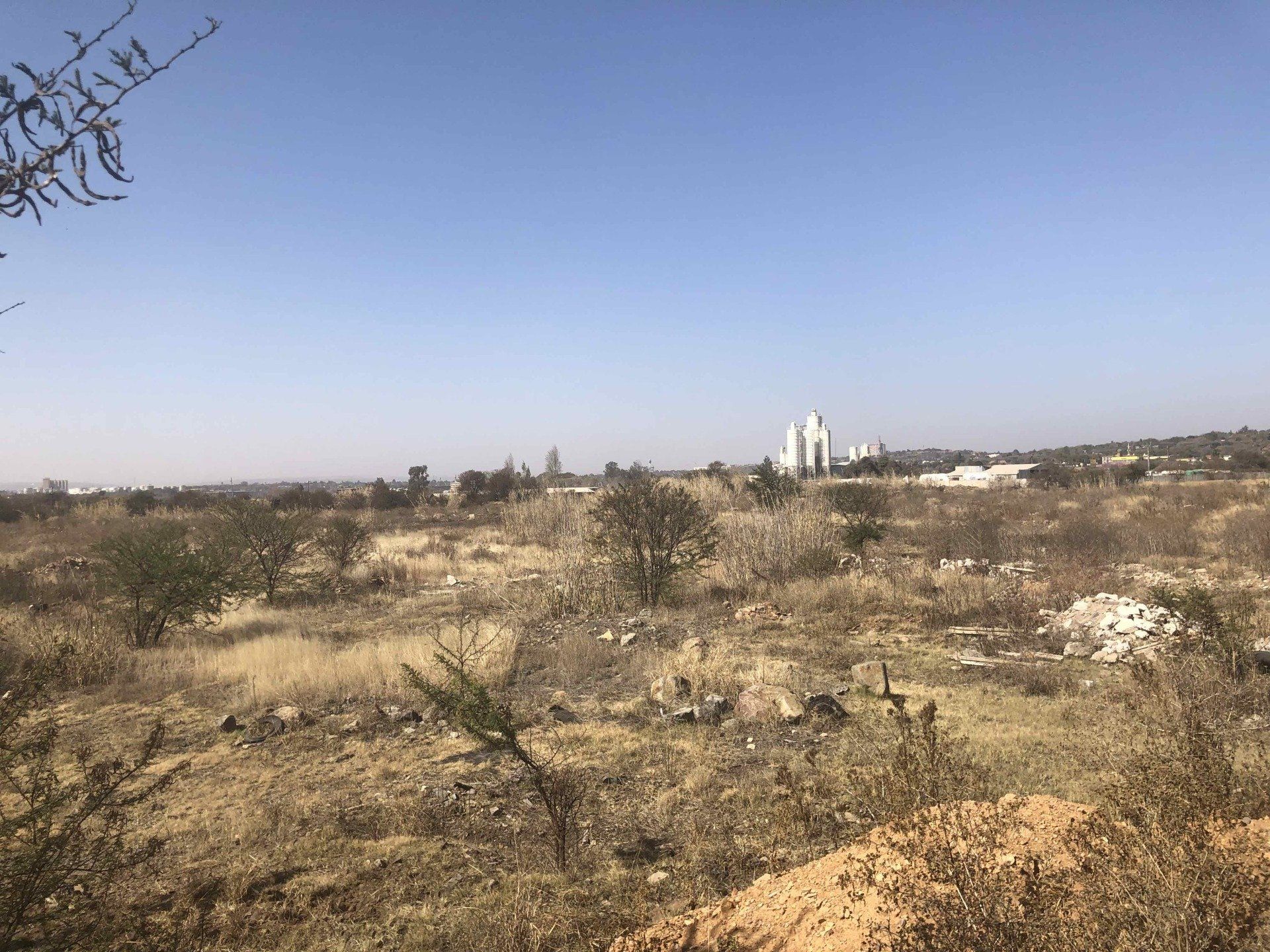 Dry, open landscape with low bushes and a distant white building under a clear blue sky.
