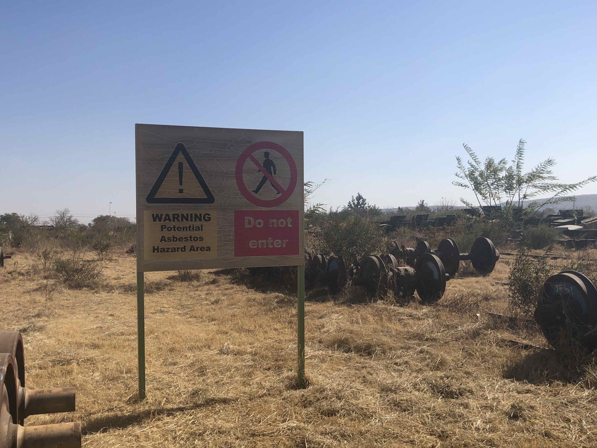 Sign in field with warning triangle and no-entry symbol, in a dry, grassy landscape on a sunny day.