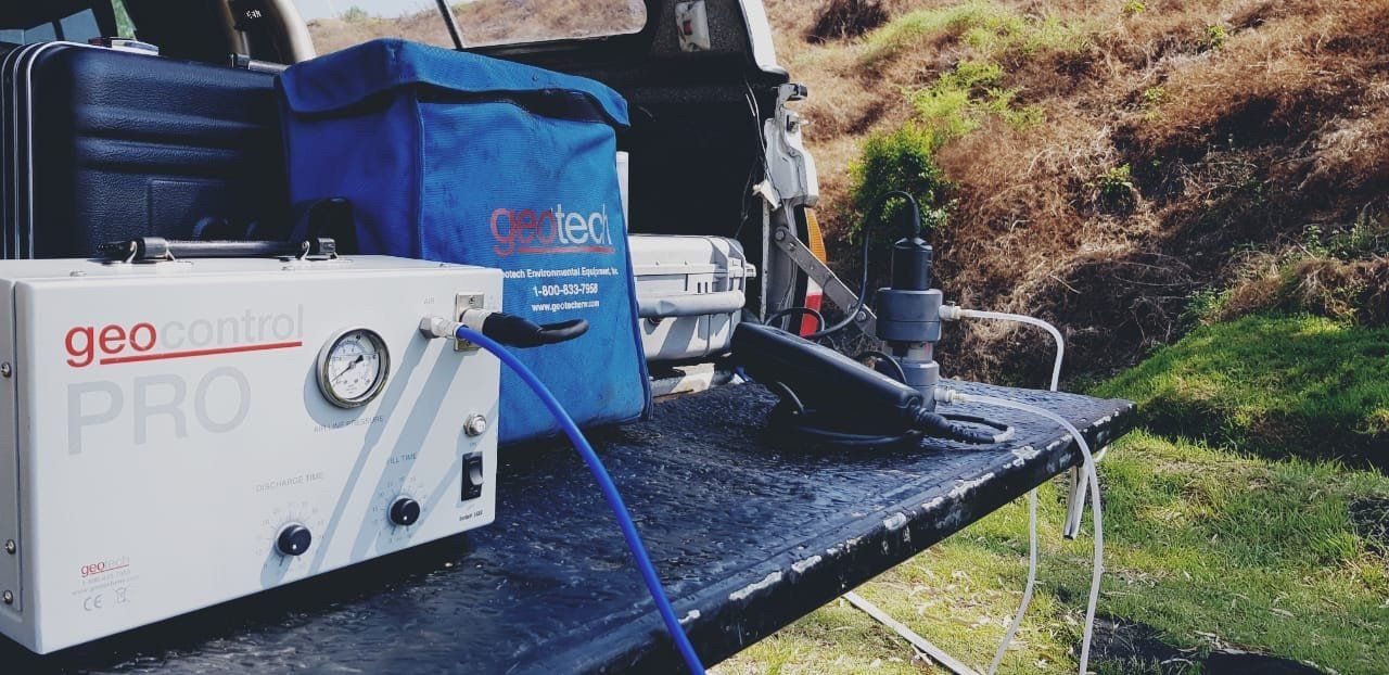 Equipment, including a gauge and blue tubing, sits on a truck bed in a natural setting.
