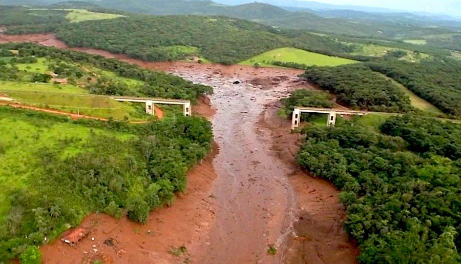 Muddy river flowing through a forested valley, under the remains of a bridge.
