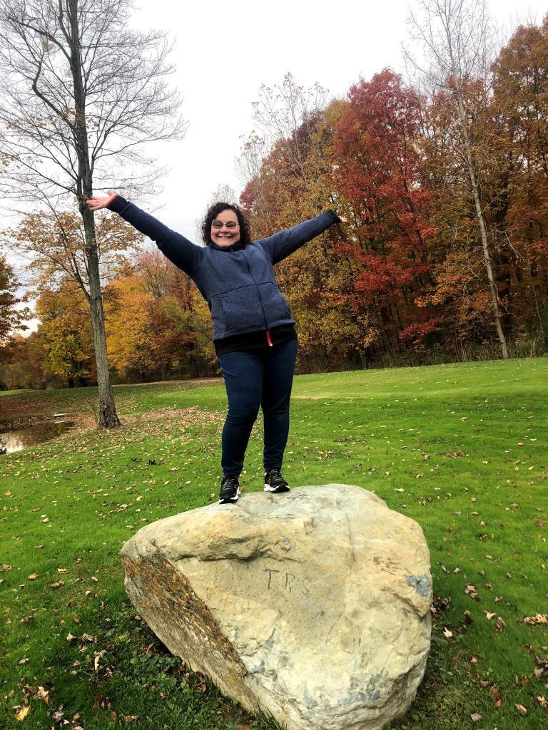 A woman is standing on a large rock with her arms outstretched.
