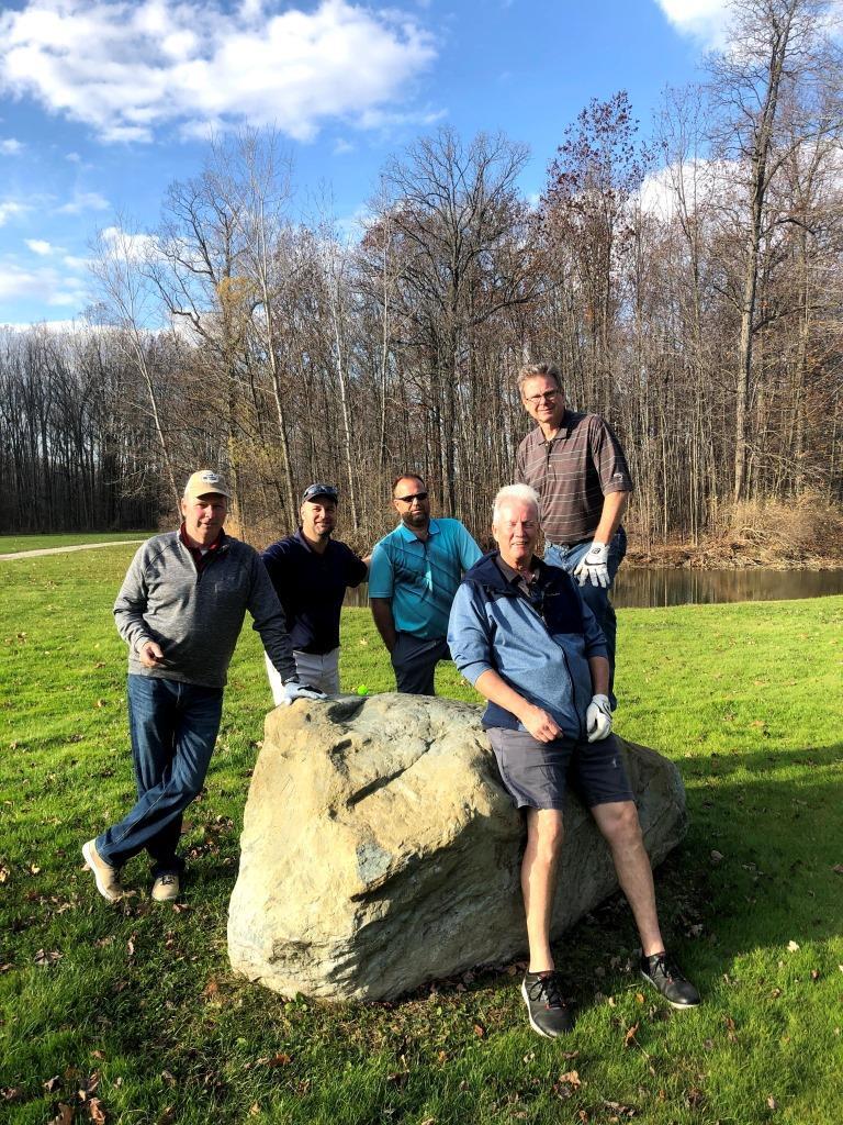 A group of men standing around a large rock in a field.