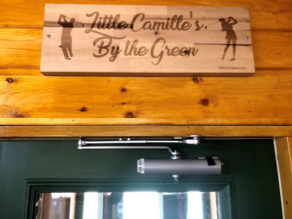 A wooden sign that says little camille's by the green.