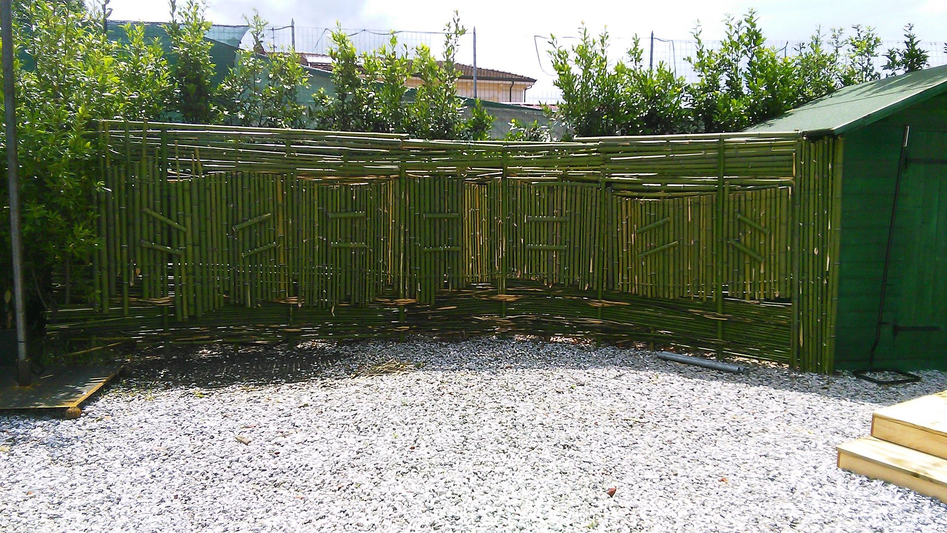 Una recinzione di legno verde a doghe crea uno schermo per la privacy a forma di L in un cortile con un pavimento di ghiaia bianca.