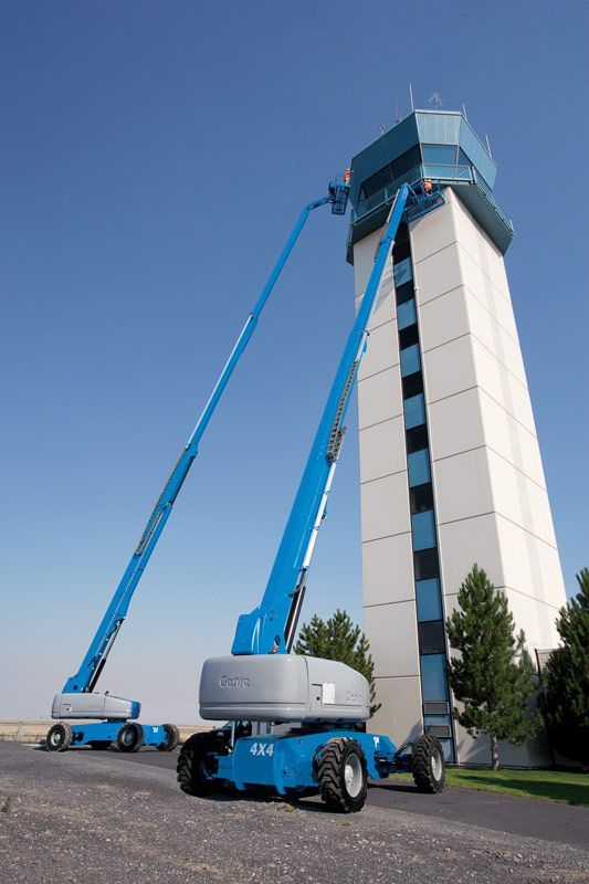 Two blue aerial lifts are parked in front of a tall building.