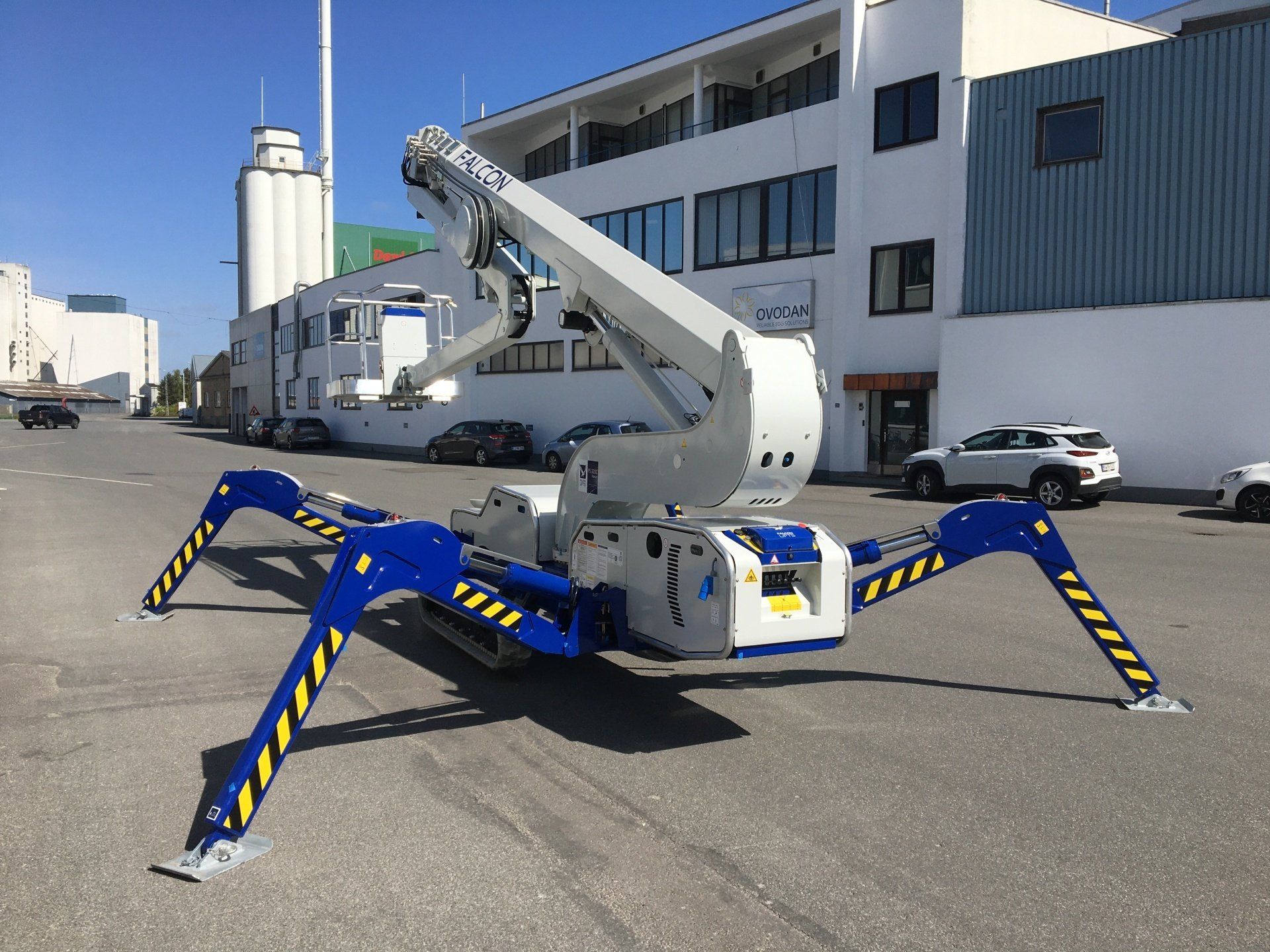 A blue and white spider lift is parked in front of a building.
