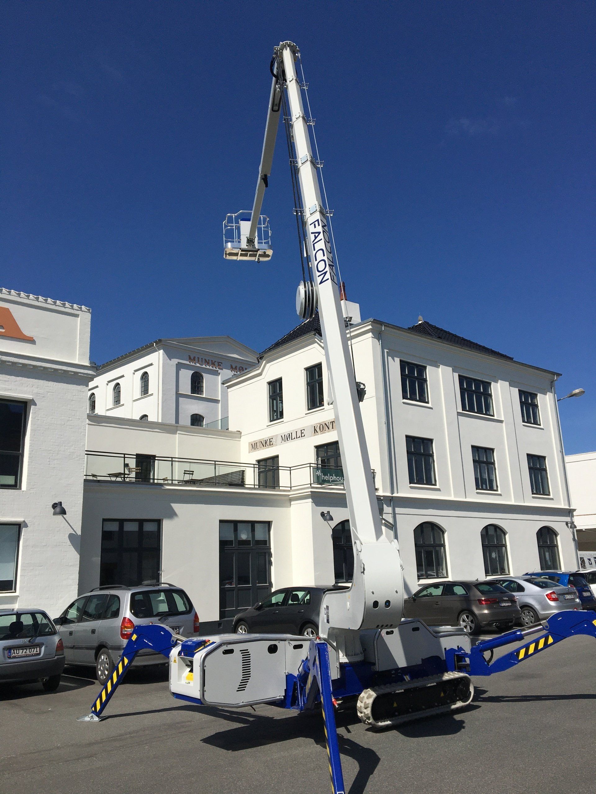 A blue and white crane is parked in front of a white building
