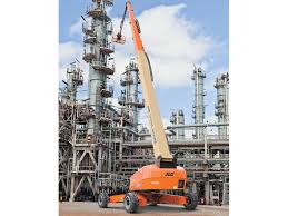 A large orange crane is parked in front of a large oil refinery.