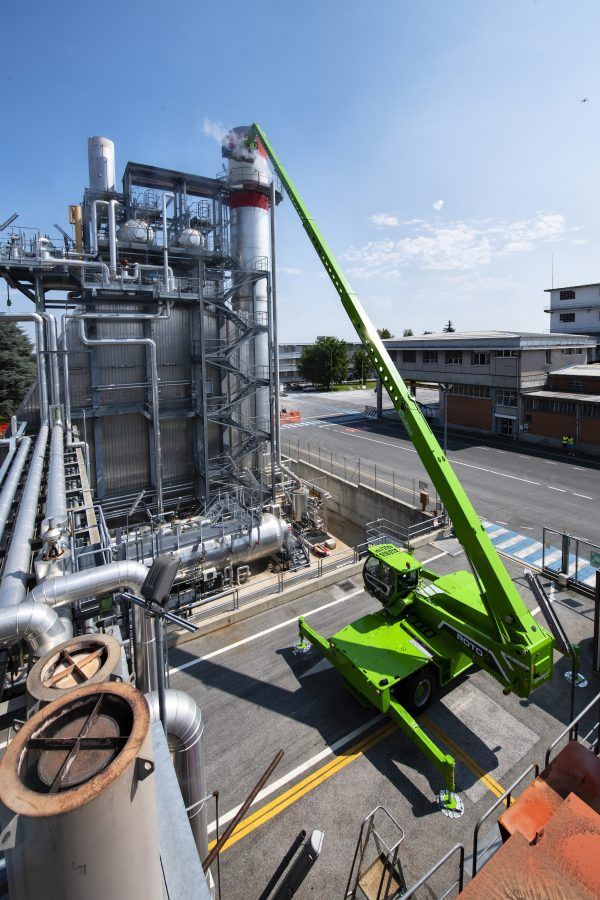 A green crane is sitting in front of a factory.