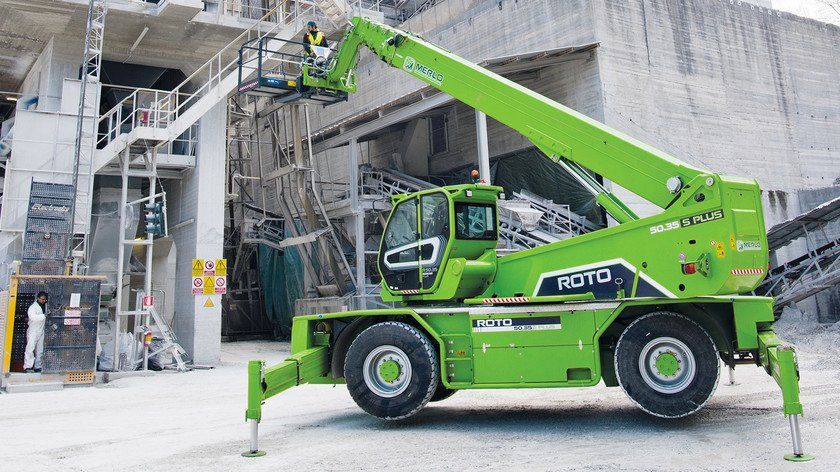 A green crane is parked in front of a building.