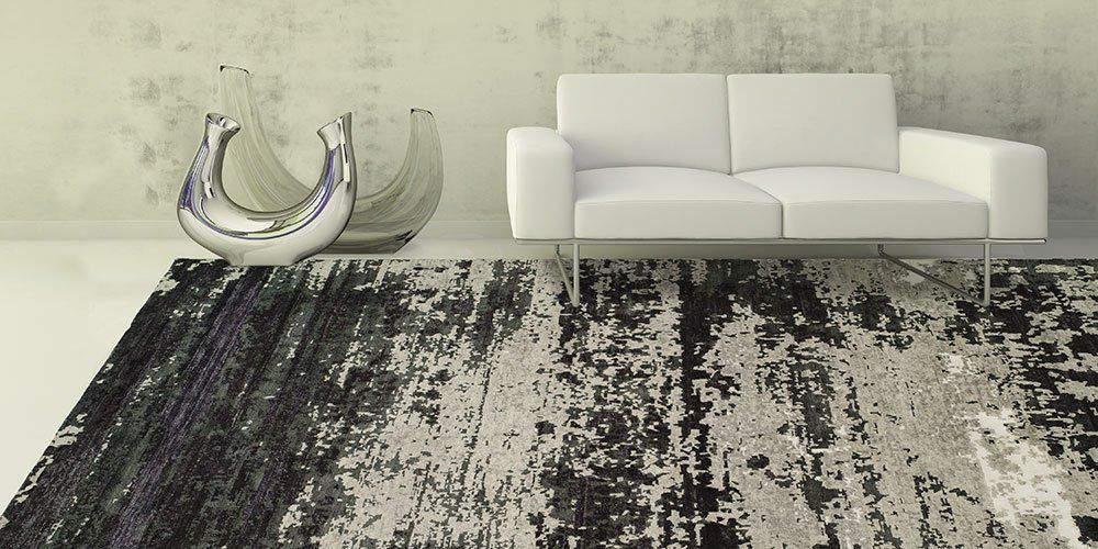 Minimalist living room with a white sofa, transparent chair, and dark patterned rug on a pale floor.