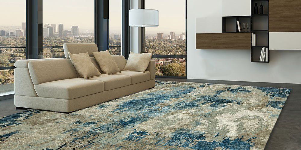 Modern living room with beige sofa, blue patterned rug, wall shelves, and city view windows