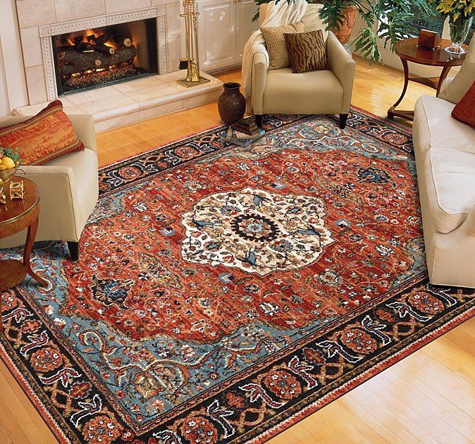 Cozy living room with a red patterned area rug, fireplace, armchairs, and light wood floors.