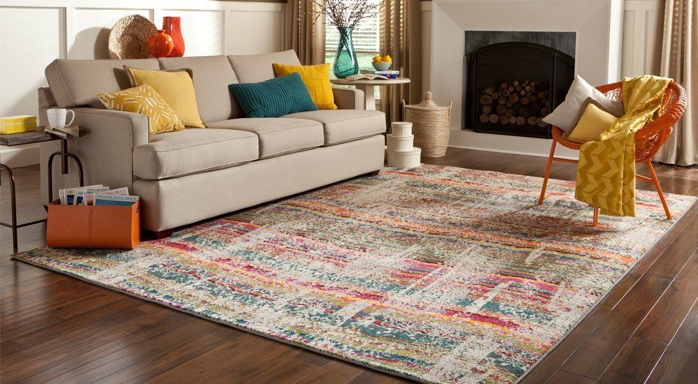 Cozy living room with beige sofa, colorful rug, fireplace, and mustard chair by a sunlit window