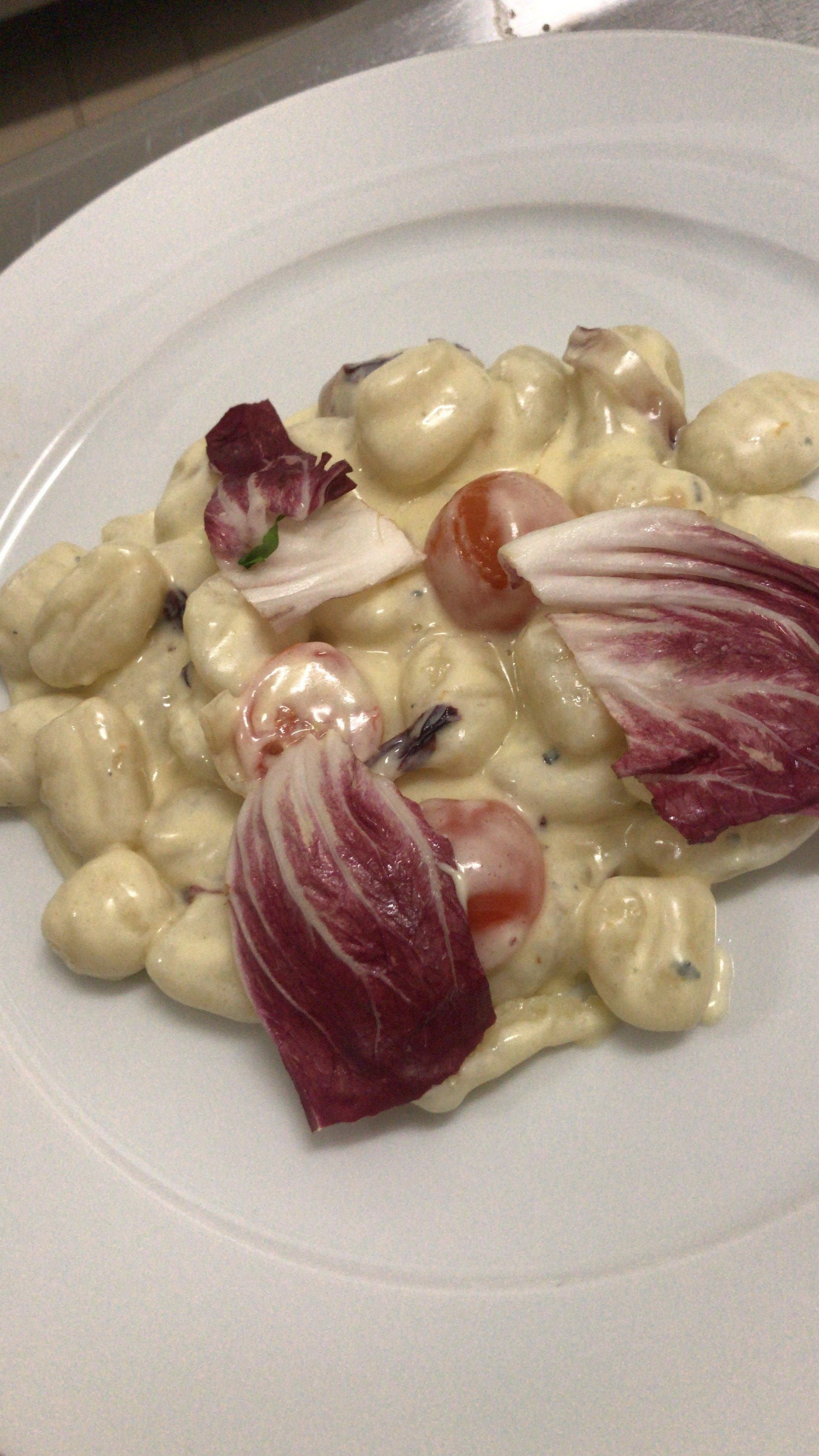 Ein weißer Teller mit Gnocchi und Gemüse auf einem Tisch.