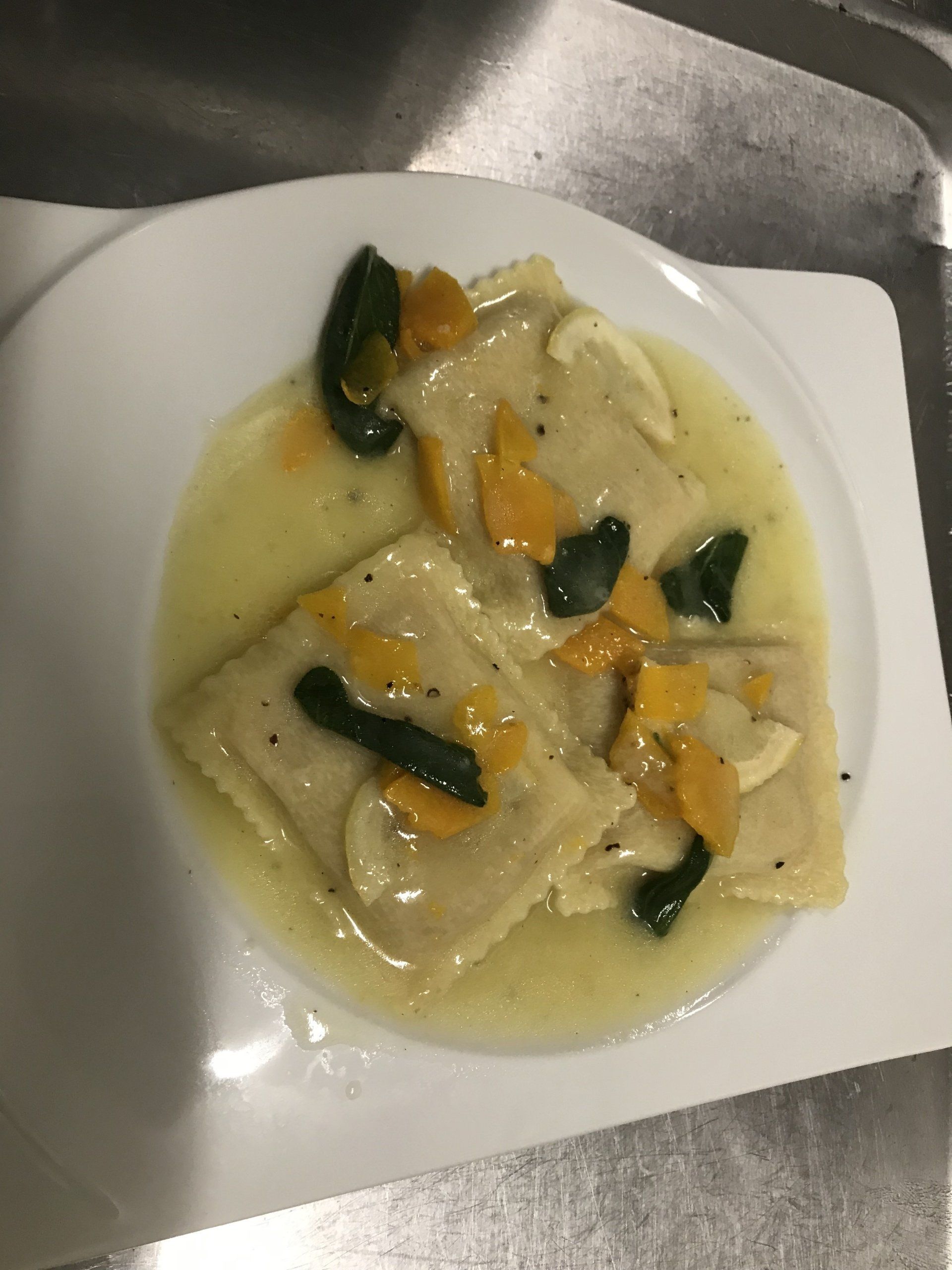 Ein weißer Teller mit Ravioli und Soße auf einem Tisch.