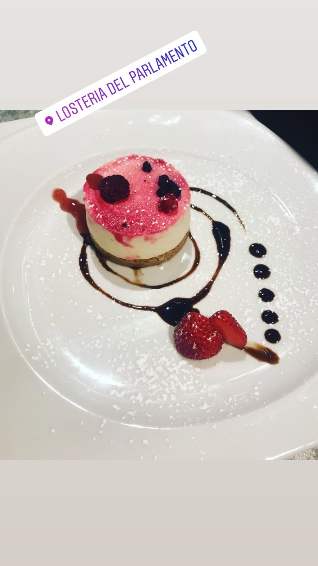 Ein weißer Teller mit einem Dessert aus Beeren und Puderzucker.
