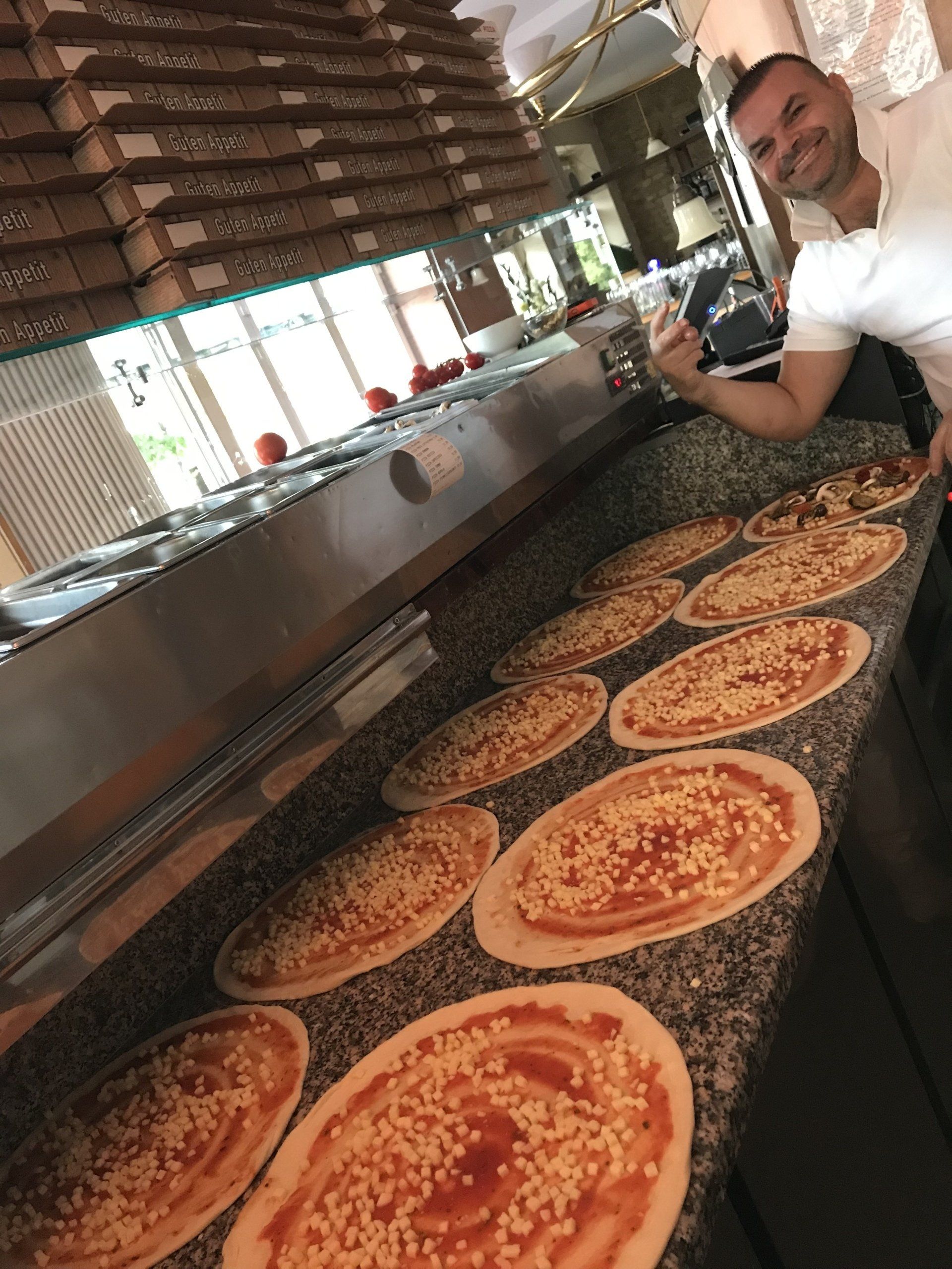 Ein Mann steht vor einer Theke voller Pizzas