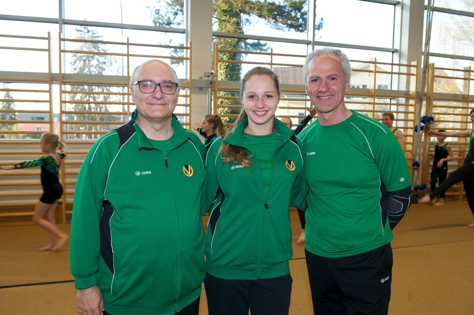 Drei Personen in grünen Hemden posieren für ein Foto in einem Fitnessstudio