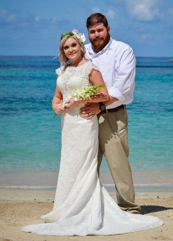 Couple in wedding attire on beach, bride in white lace dress, groom in white shirt and khakis.