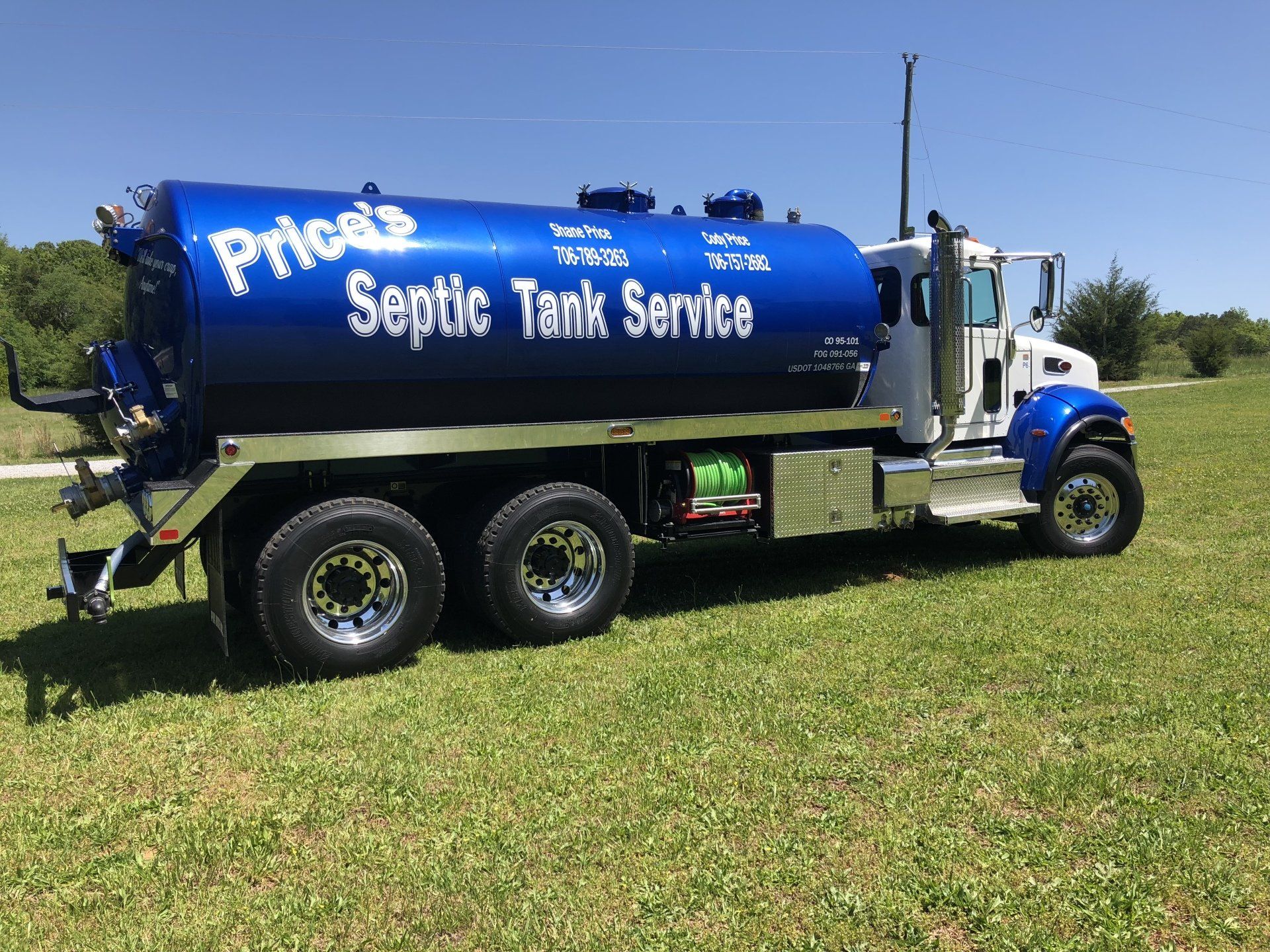 Blue and white Price's Septic Tank Service truck on grass.
