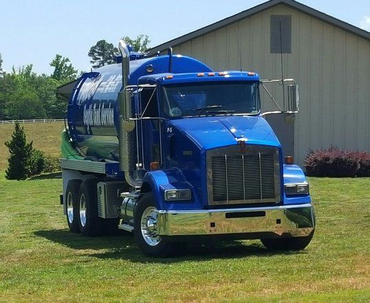 Blue septic truck parked on grass in front of a building.