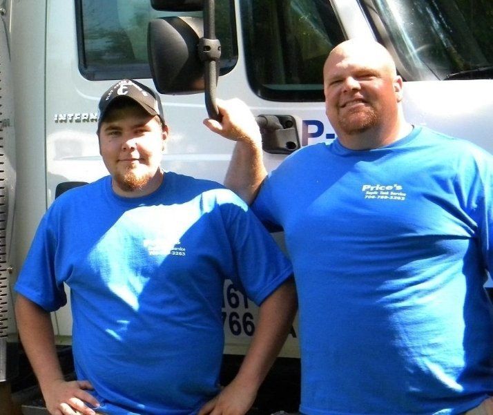 Two men in blue shirts stand in front of a white truck. One man holds up the truck's mirror.