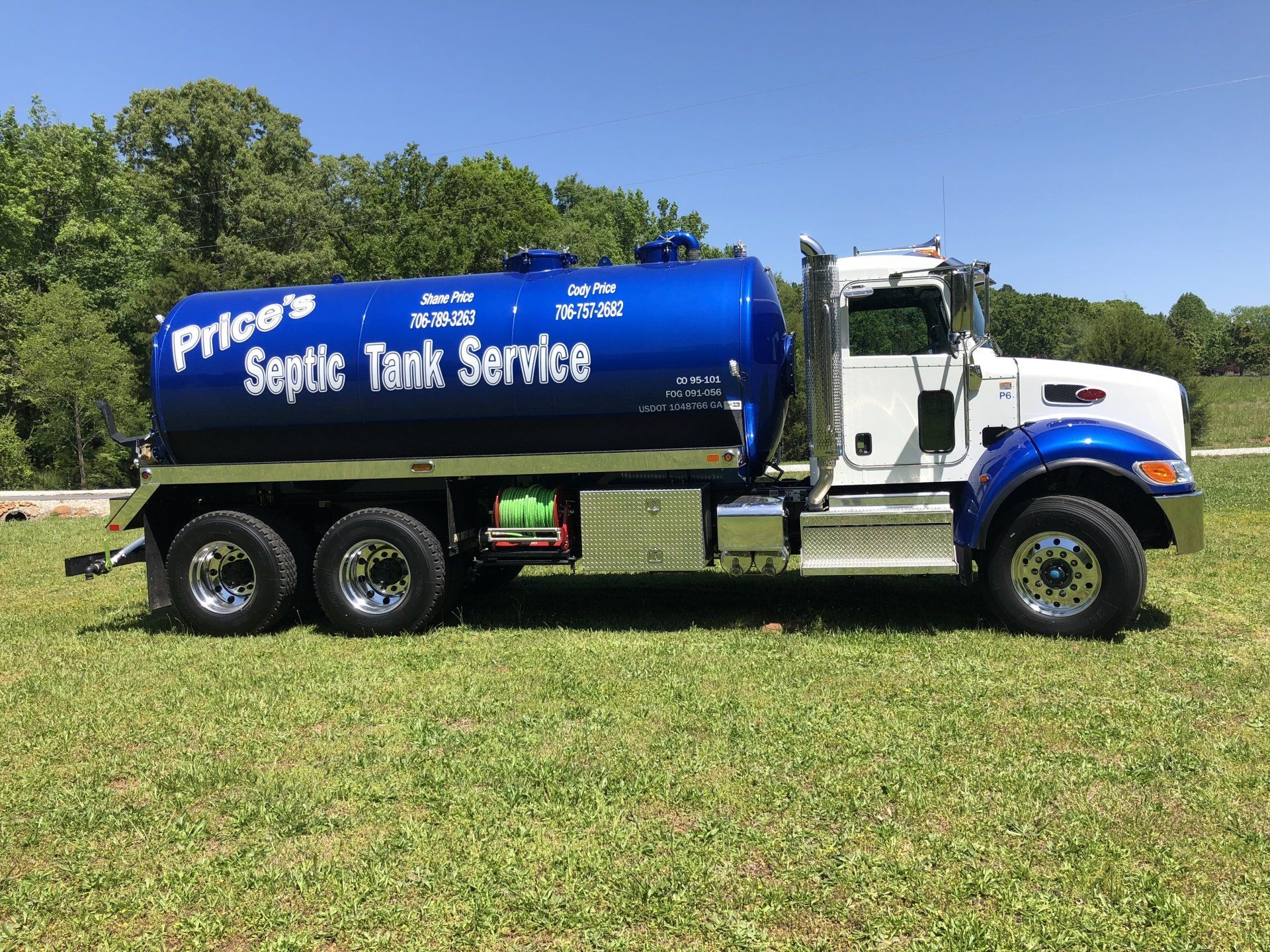 Blue and white septic tank truck parked on green grass, with the words 