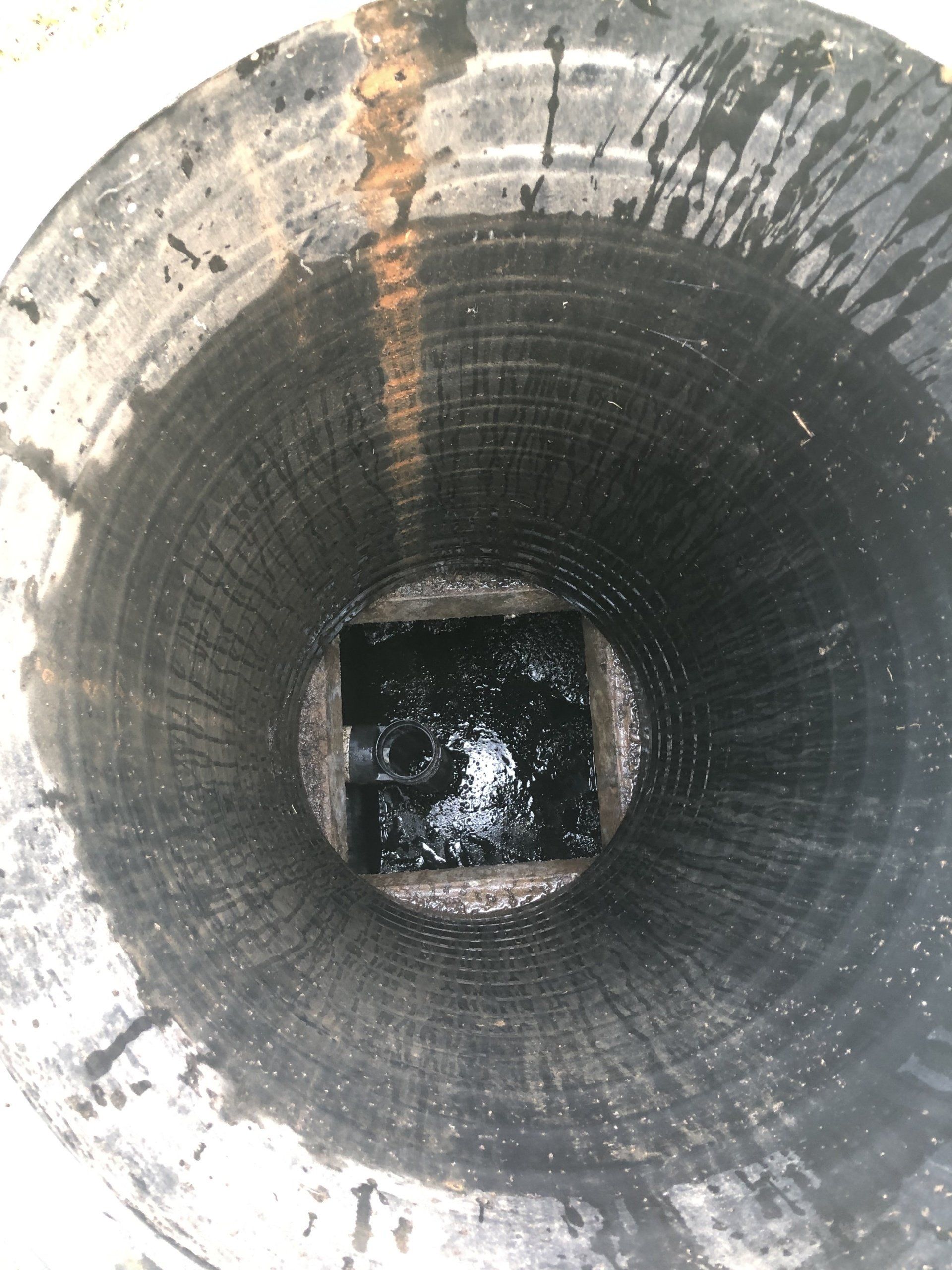 Looking down into a cylindrical, dark, possibly concrete, hole. A square shape is at the bottom.