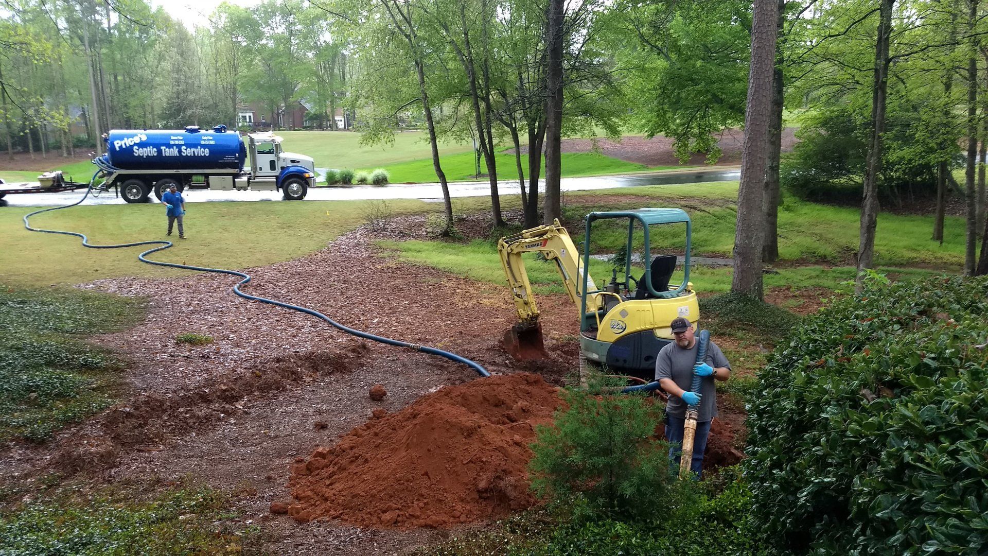 Septic tank service: truck, excavator, and workers in a yard.