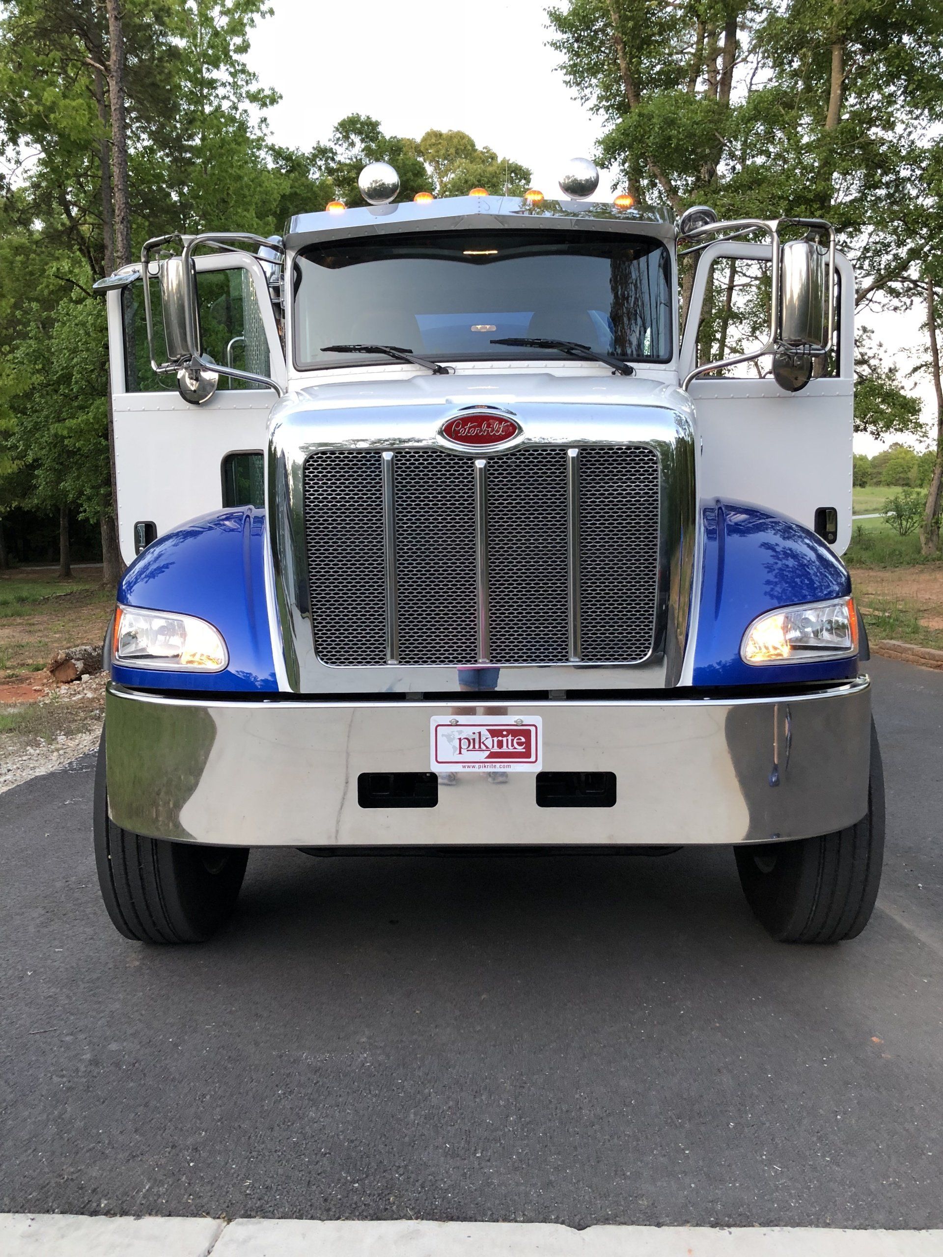 Blue and silver Peterbilt truck with open doors, parked on a paved driveway.