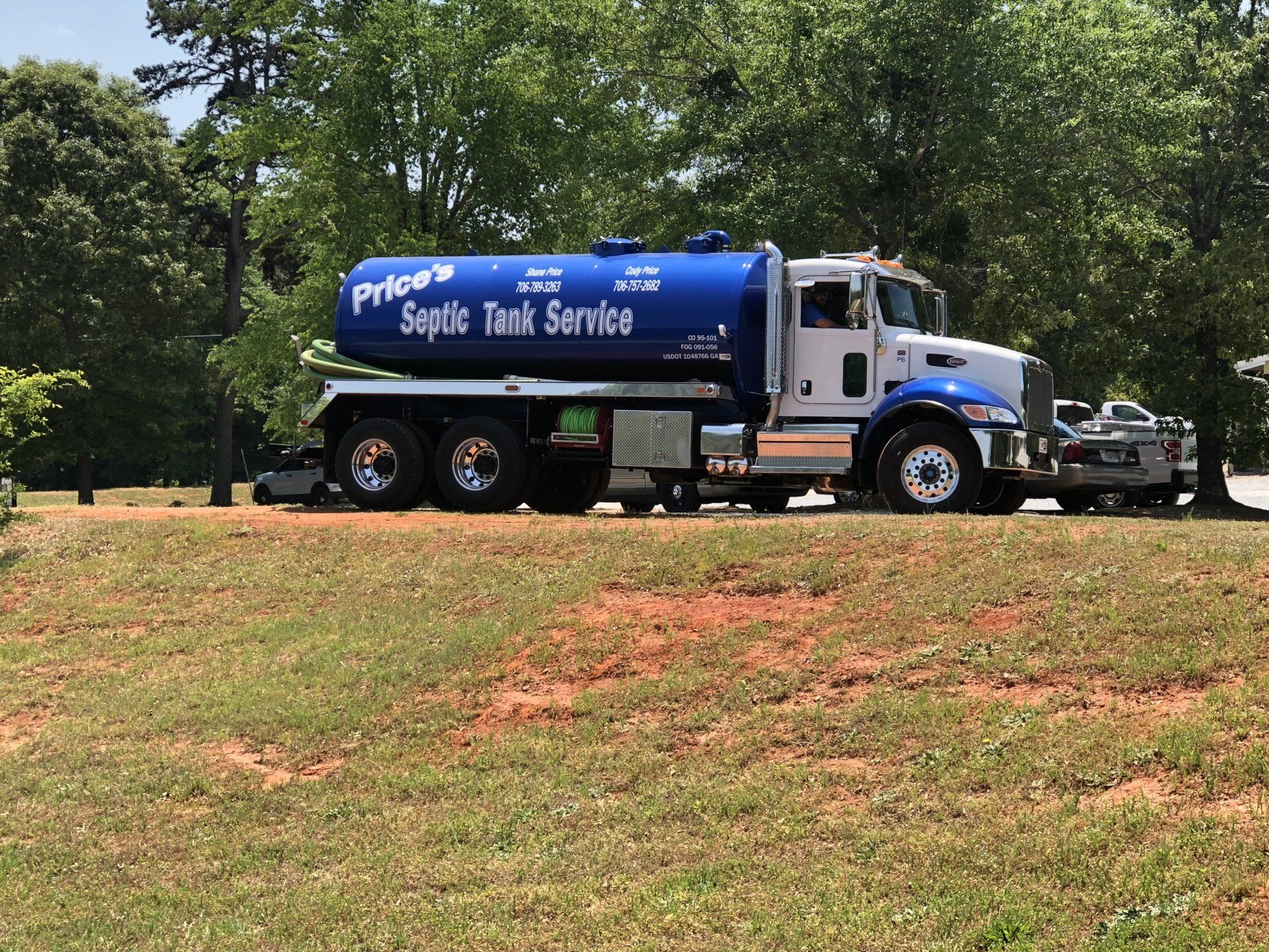 Septic tank service truck parked on grassy hill, blue tank with company logo.