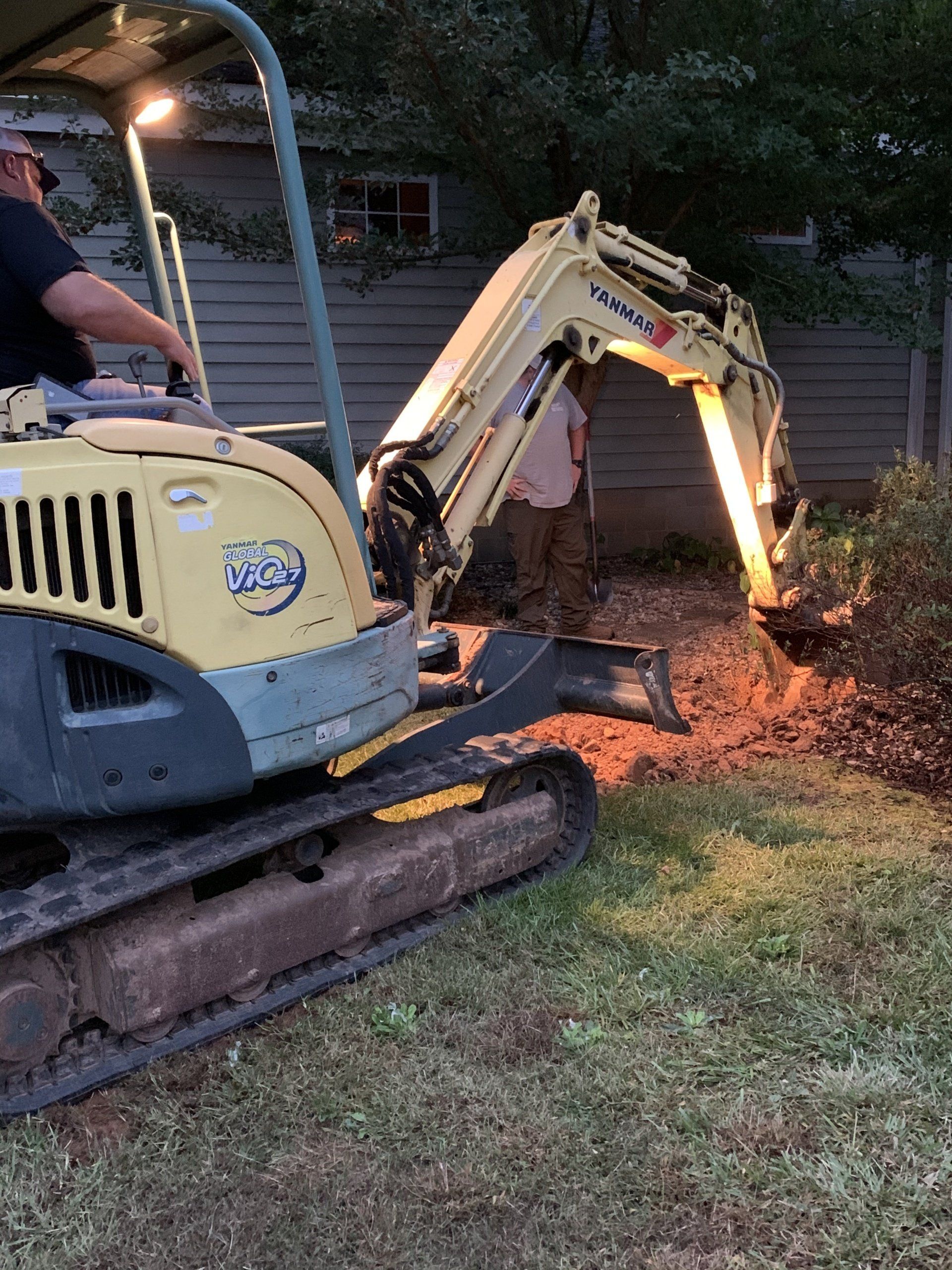 Mini excavator digging in a yard at night with a person operating it.
