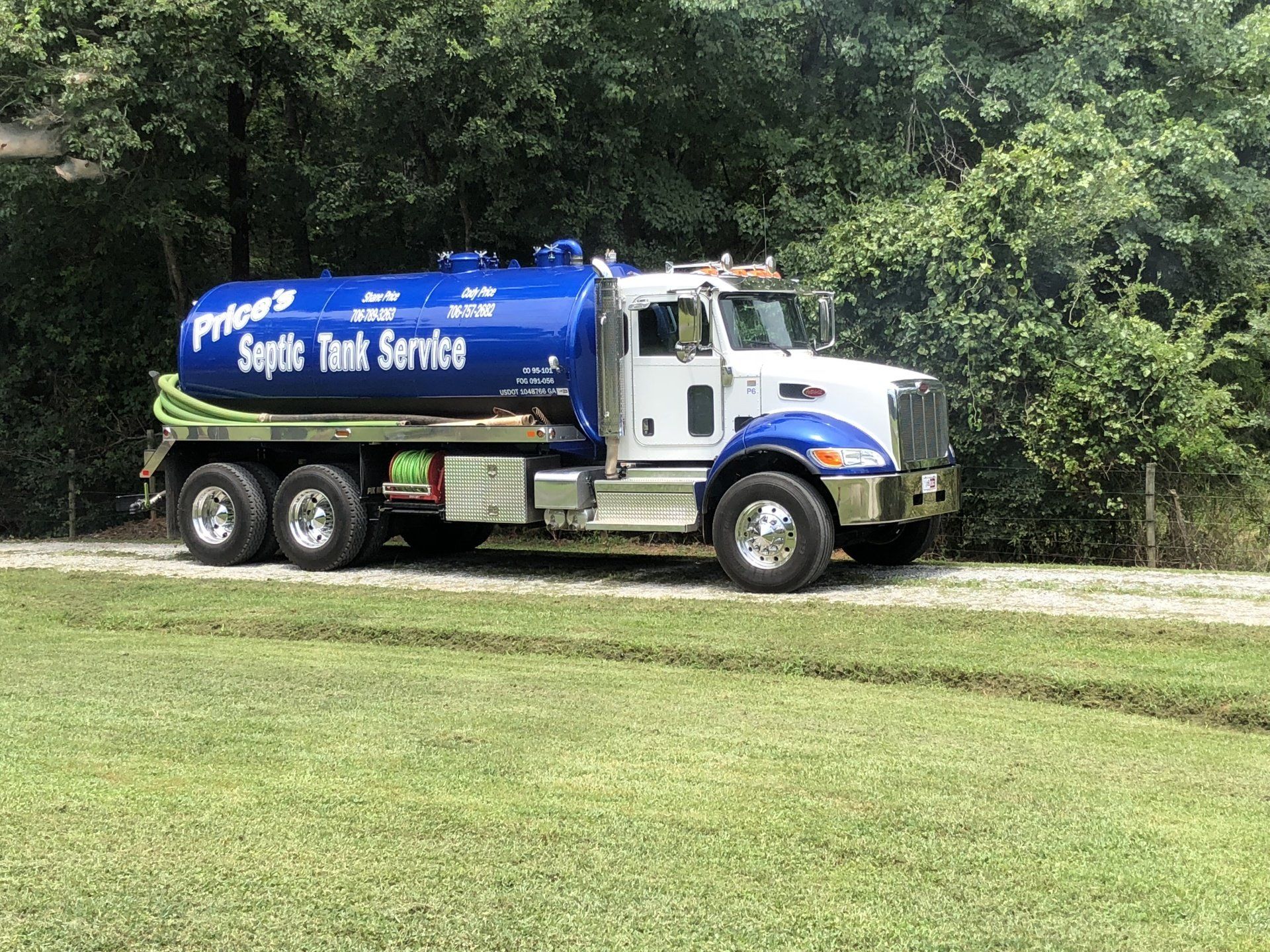 Blue and white septic tank service truck on a grassy area, trees in the background.