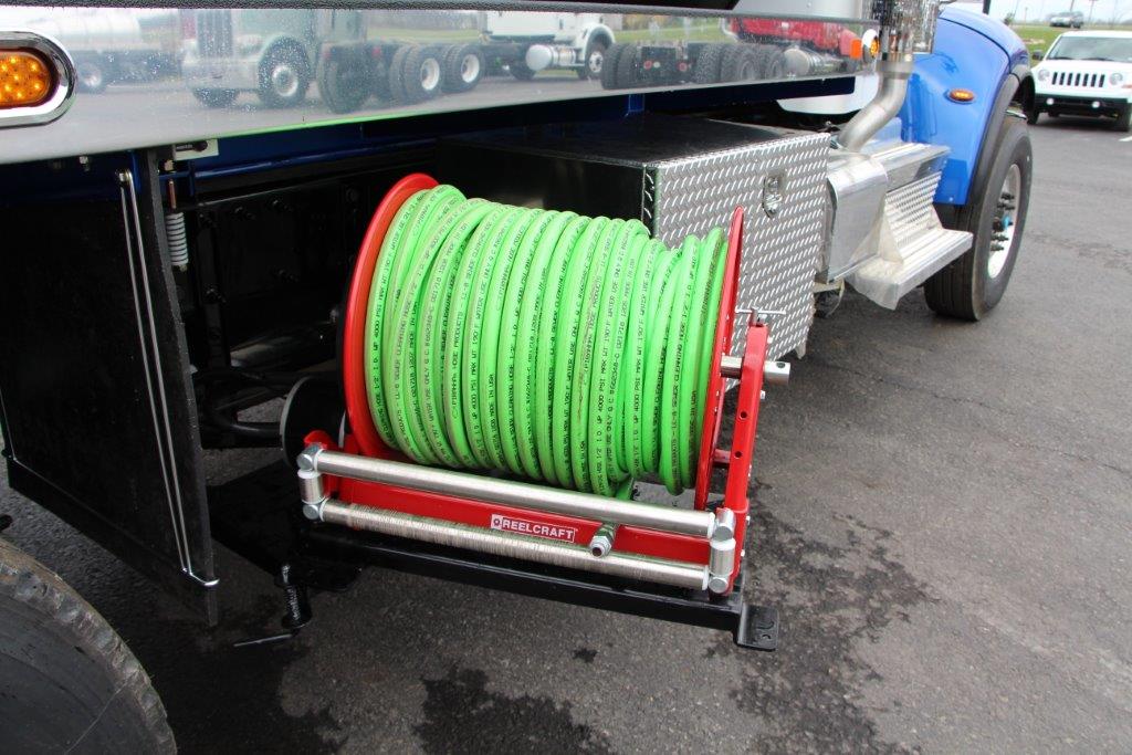 Green hose reel mounted on the side of a truck, red frame, black truck bed, outdoor setting.