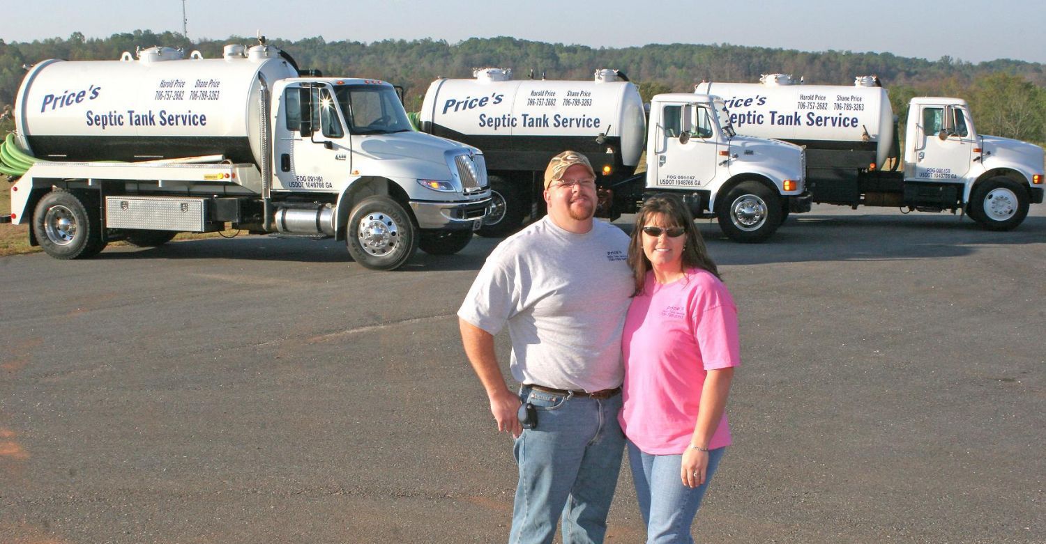 Couple standing in front of three septic tank service trucks; sunny day.