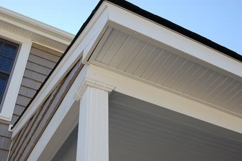 A close-up view of the white exterior trim, soffit, and column on the corner of a house with gray siding.