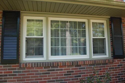 A white triple-pane window with a grid pattern, flanked by black shutters on a red brick exterior wall.