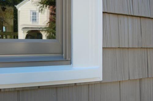 Brown Siding With White Window Frame — Siding in Newport News, VA A close-up view of a white window frame set into light gray cedar-style siding, reflecting a neighboring house.