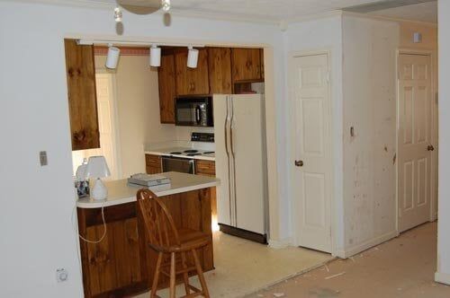 A kitchen with wooden cabinets, a white refrigerator, a breakfast bar with a wooden stool, and two closed white doors.