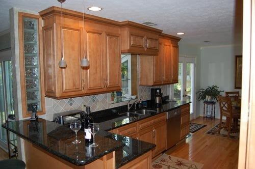 A kitchen with wooden cabinets, black granite countertops, a stainless steel dishwasher, and a glass block accent wall.