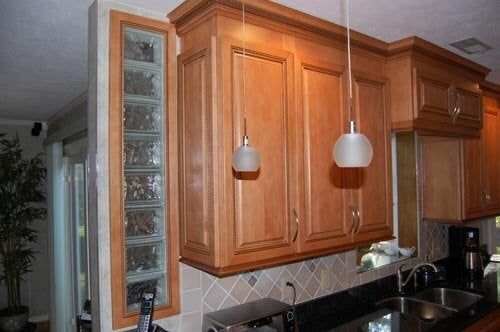 A kitchen featuring light wood cabinets, two hanging pendant lights, and a vertical glass block window inset in the wall.