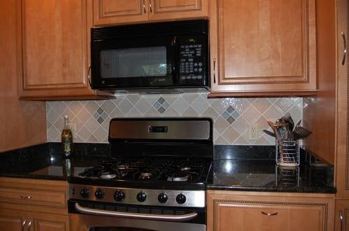 A kitchen scene with wooden cabinets, a black microwave, a gas stove, and a diamond-patterned tiled backsplash.